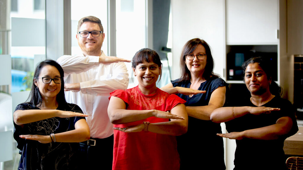 Group of smiling CSG employees making the equality arm gesture