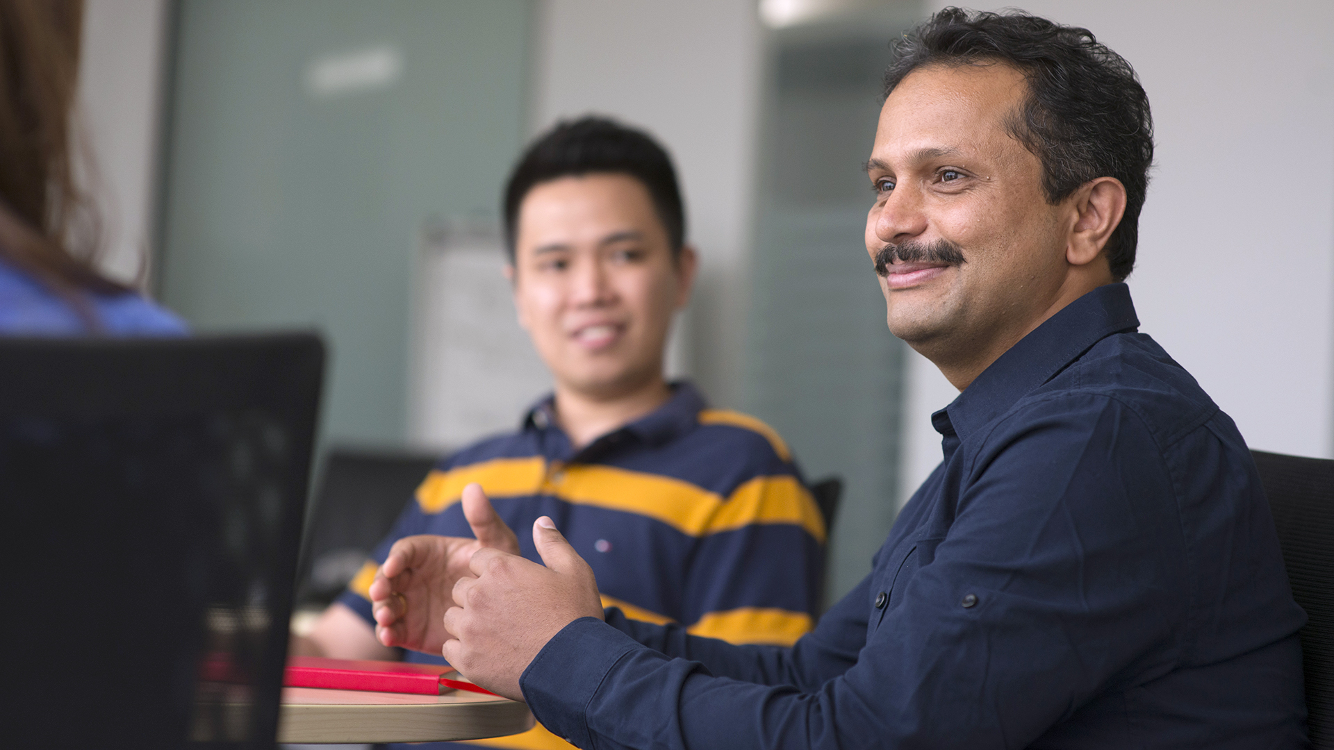 A smiling male CSG employee participating in a team discussion in a conference room.