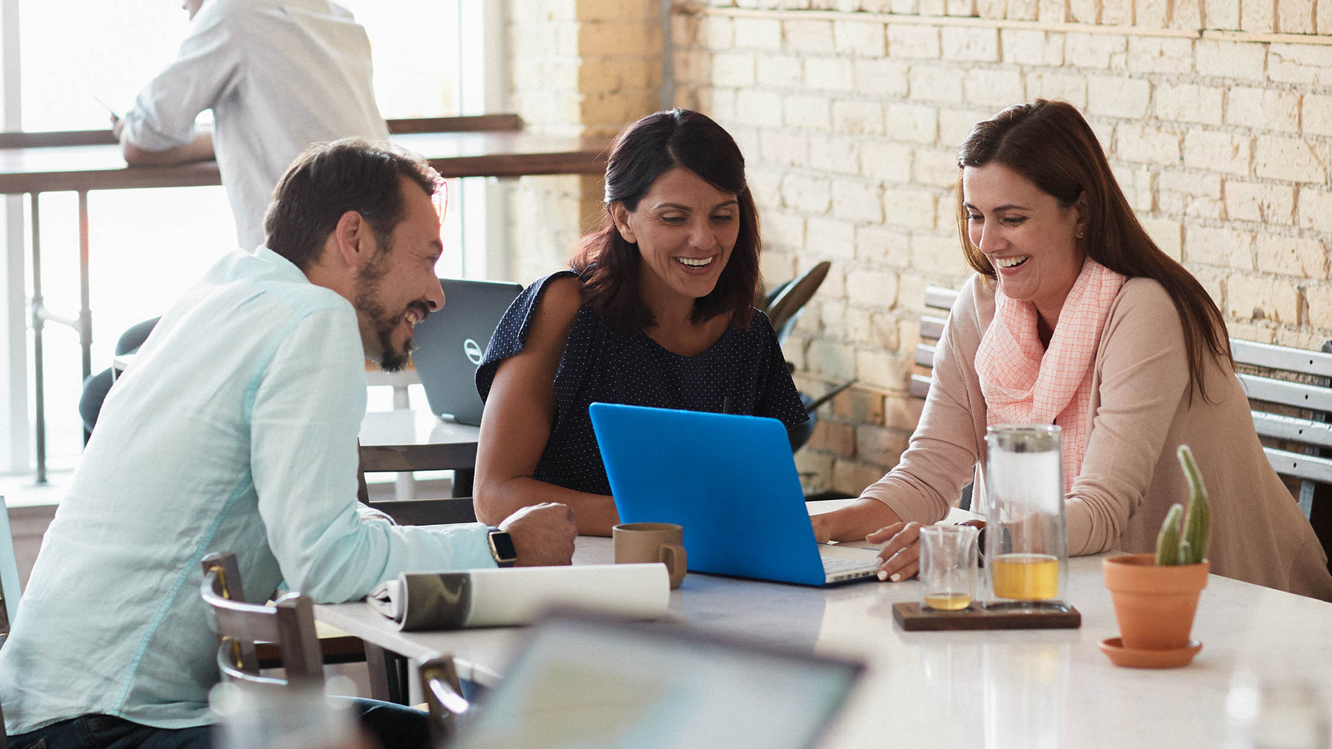 Three colleagues laughing and having a discussion while sitting around a laptop at a coffee shop table