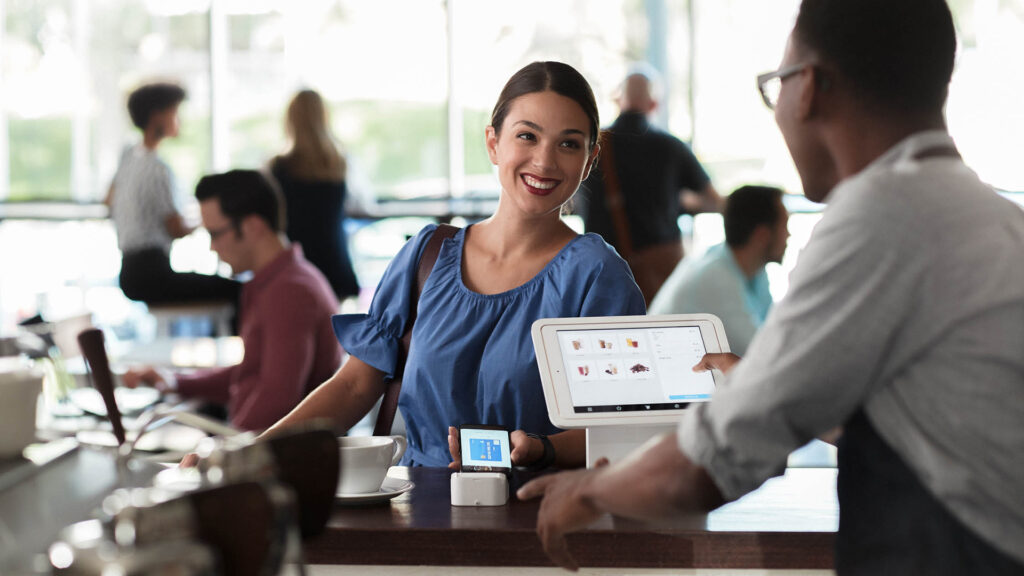 Woman smiling while using her smartphone to make a payment at coffee shop