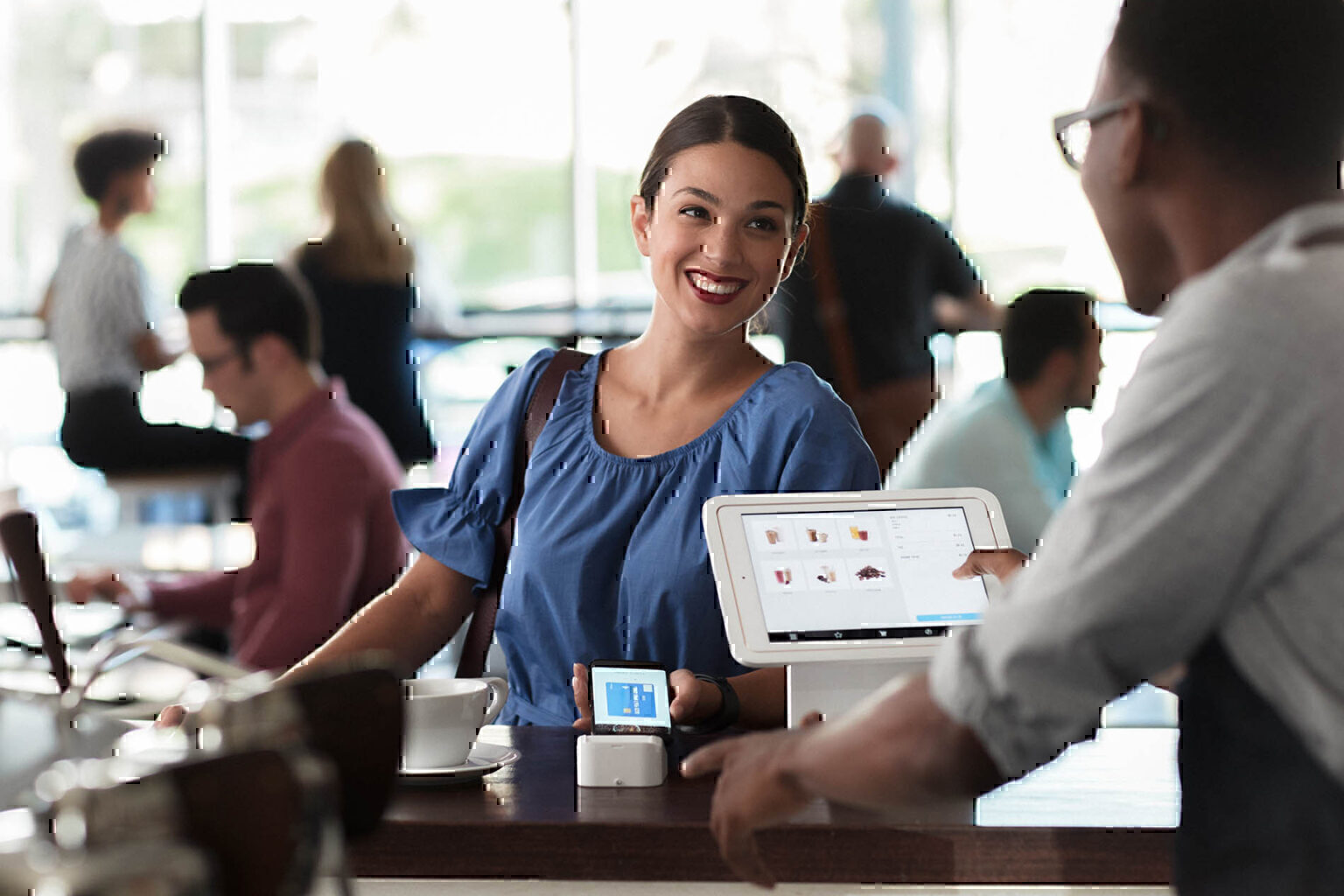 Woman smiling while using her smartphone to make a payment at coffee shop