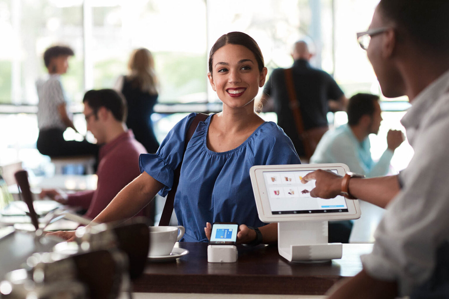 Woman smiling while using her smartphone to make a payment at coffee shop