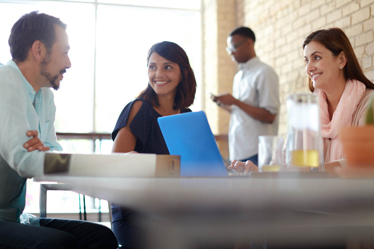 Three colleagues laughing and having a discussion while sitting around a laptop at a coffee shop table