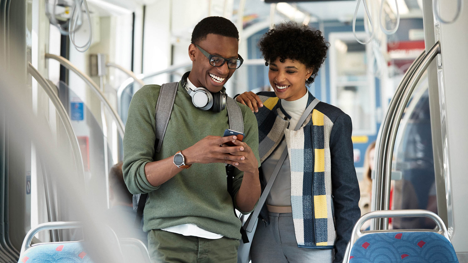 Man and woman laughing while staring at smartphone on subway