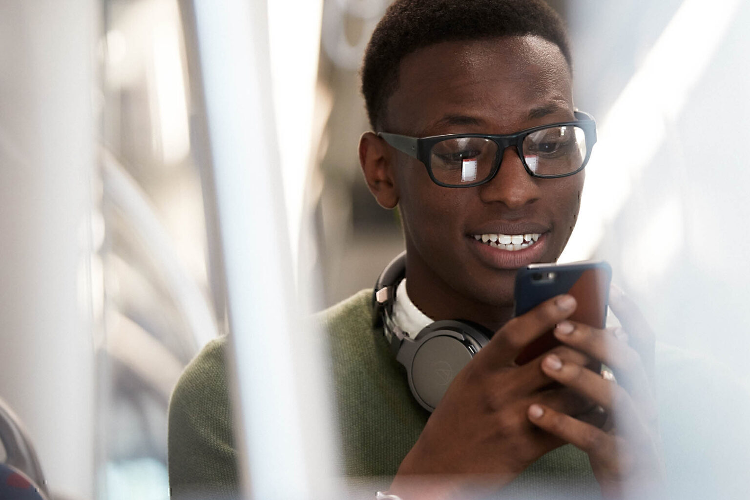 Man grinning while looking at his smartphone on the subway