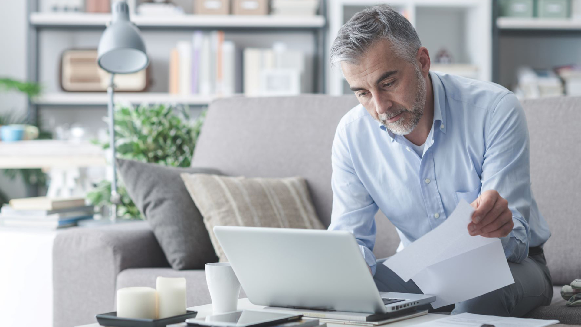 Businessman on a computer at home while checking paper billing statements.