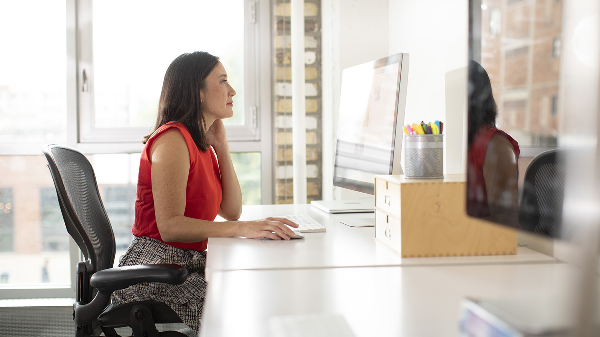 A wide shot of a woman sitting in an office chair and looking at her computer.