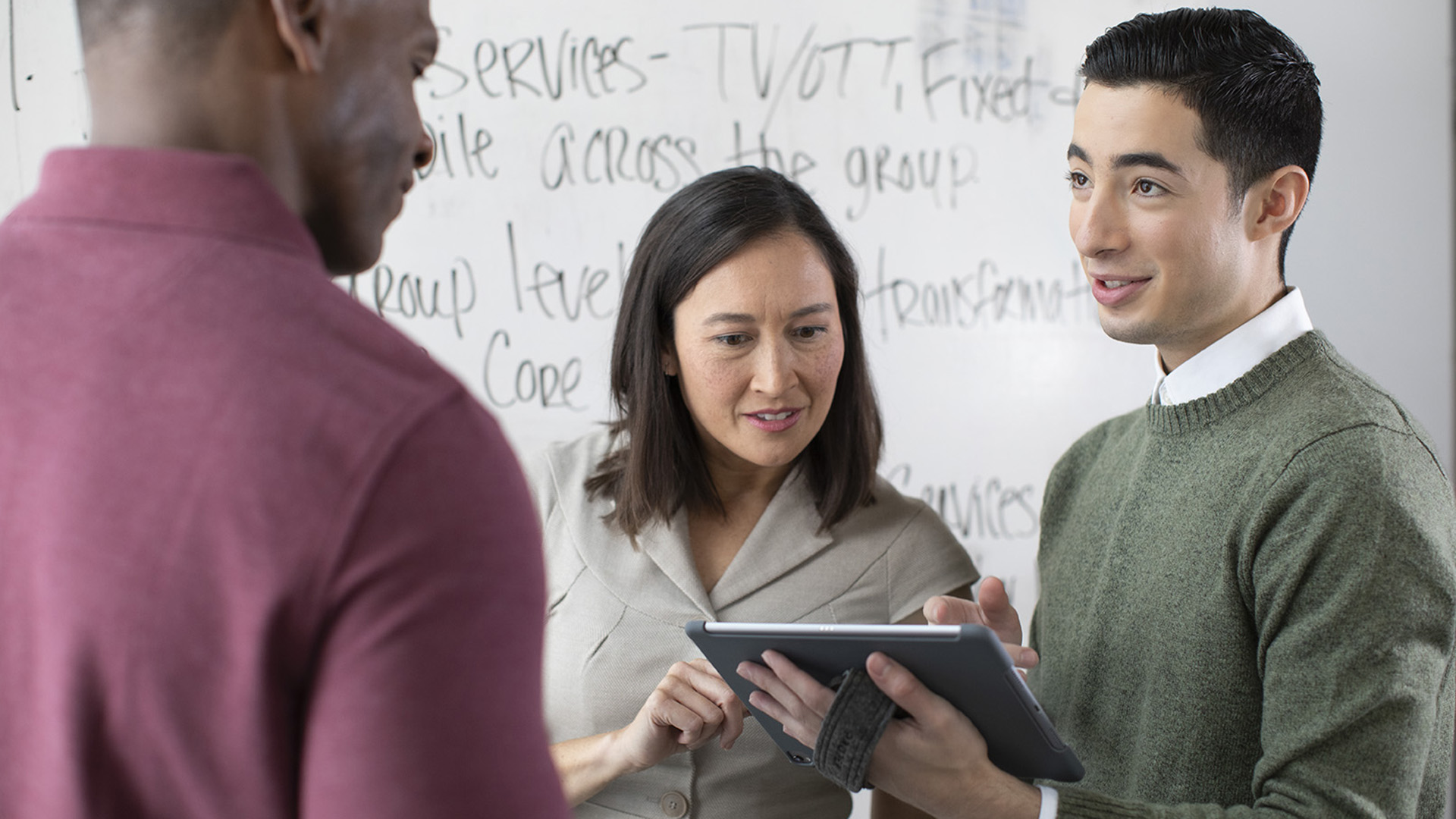 Office workers look at a tablet and talk in front of a whiteboard.