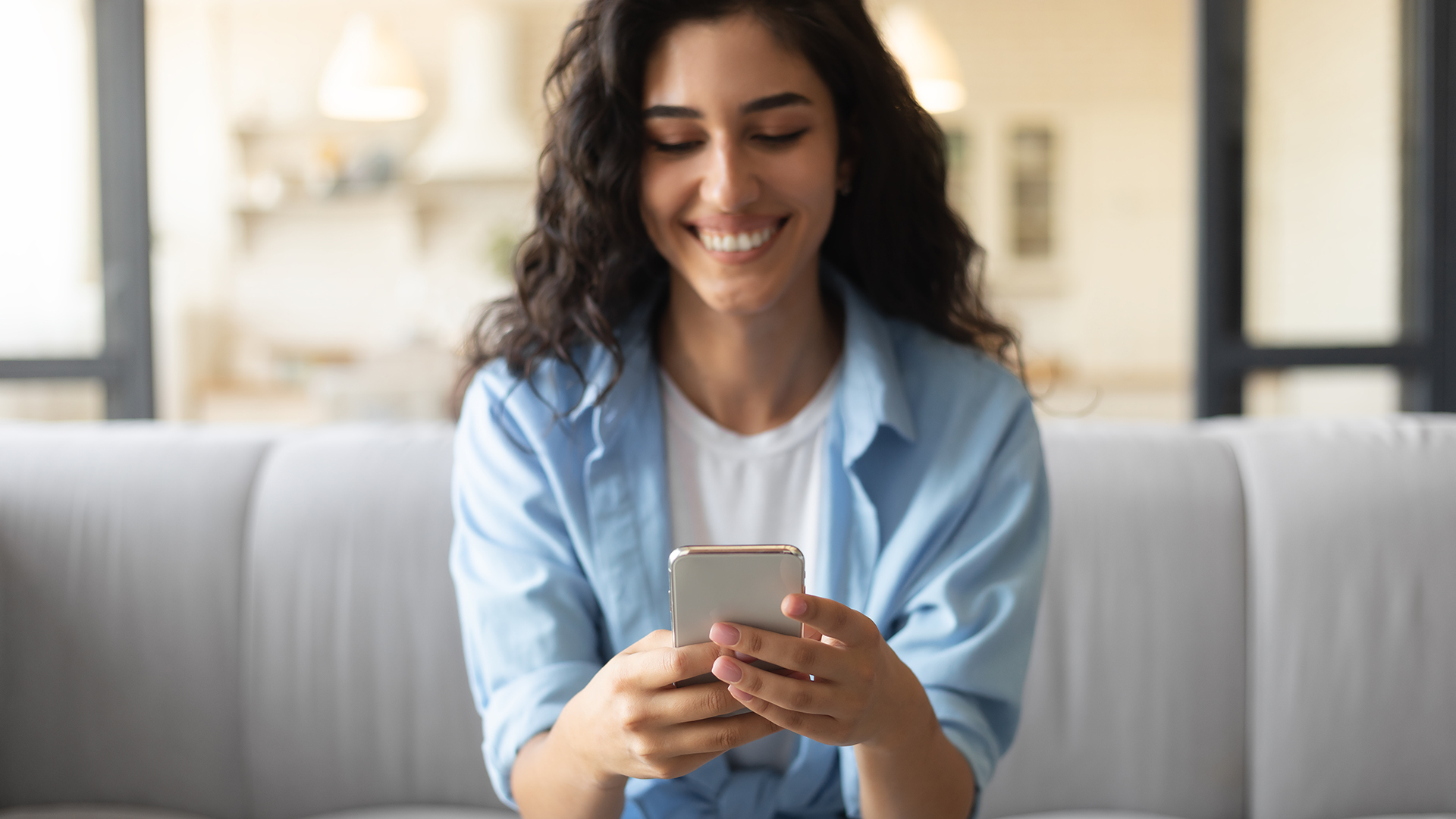 A young brunette woman using her smartphone while sitting on the couch.