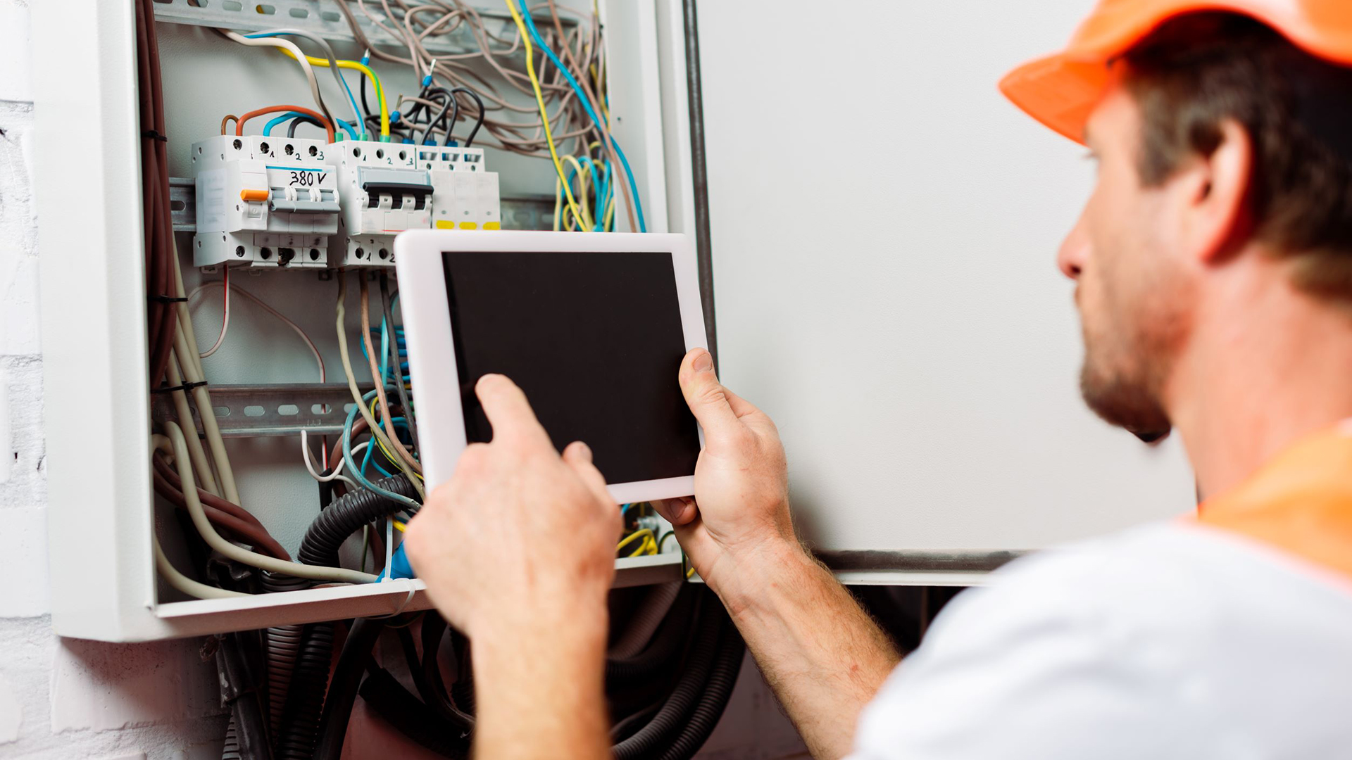 Selective focus of an electrician examining a breaker box using a digital tablet.