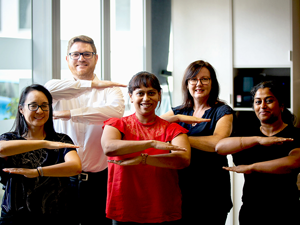 Group of smiling CSG employees making the equality arm gesture