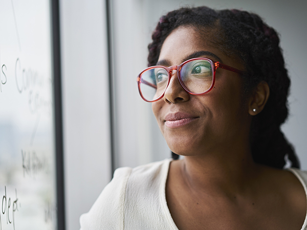 Woman in glasses staring hopefully out the window of a conference room