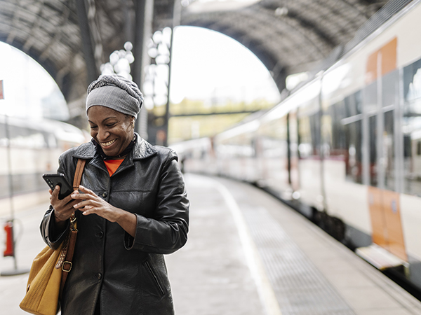 Woman smiling while using her smartphone on the platform at the train station.