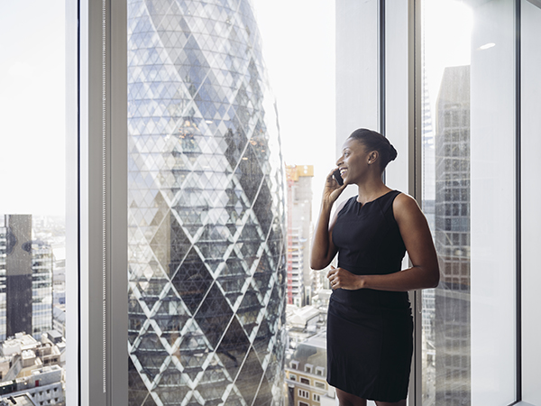 Smiling Black executive standing at window and using phone