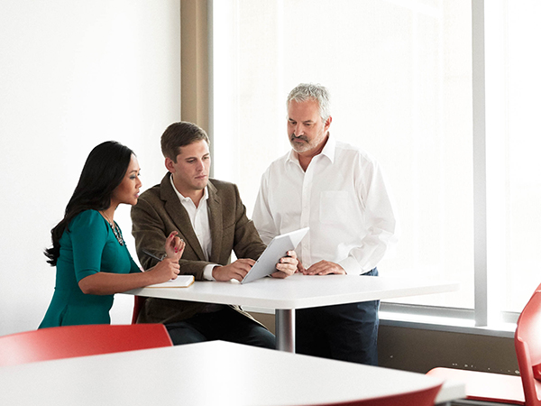 Two businessmen and one businesswoman working together while using a tablet in a conference room