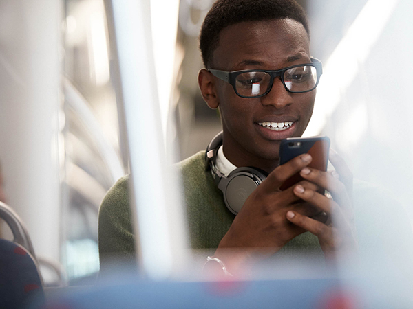 A young man riding a light rail train, looking down at his phone with anticipation