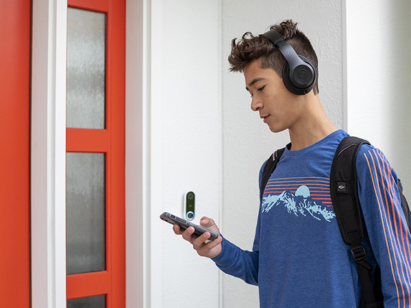 A teenage boy wearing a backpack and headphones checks his phone while entering his house