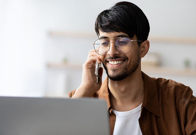 Smiling man on phone with laptop on desk.