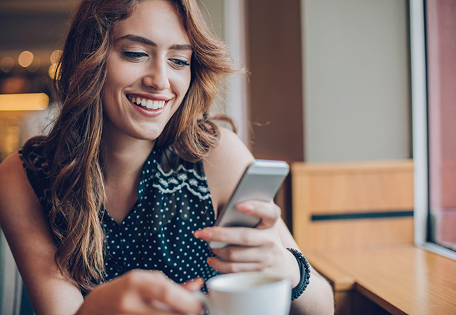 Smiling young woman in a cafe looking at her phone and holding a coffee cup