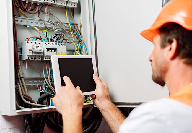 Selective focus of an electrician examining a breaker box using a digital tablet.
