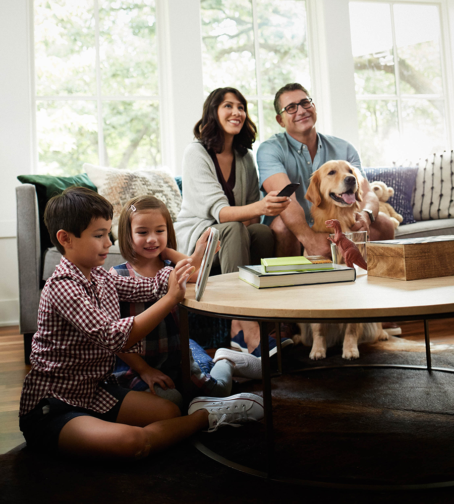 Family with two children and a dog using digital devices in the living room.