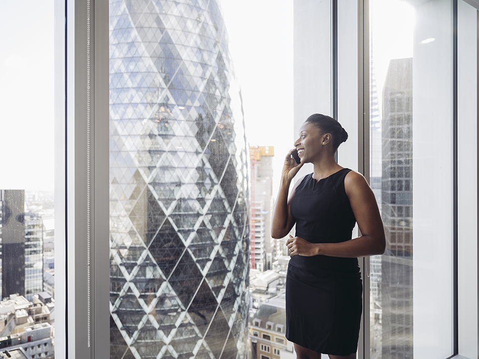 Businesswoman standing at the window in her office while using her phone