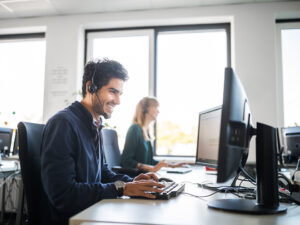 A smiling customer service representative is using a computer at his desk.
