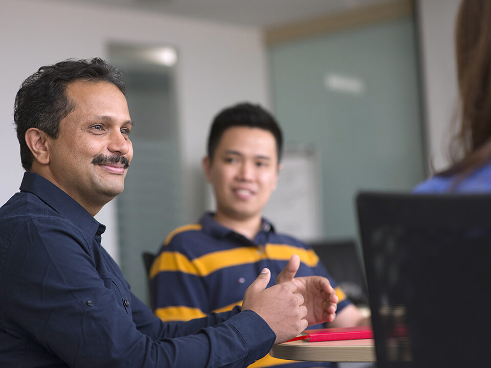 A smiling male CSG employee participating in a team discussion in a conference room.