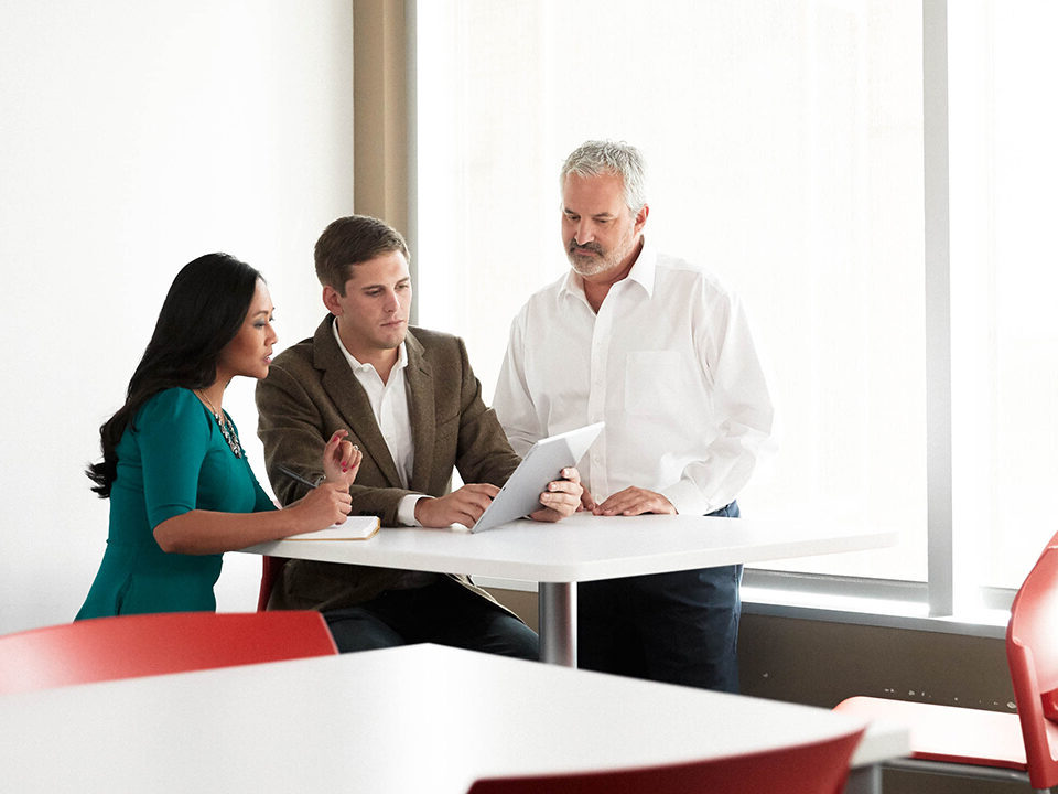 A group of office worker collaborate and look at information on a tablet.