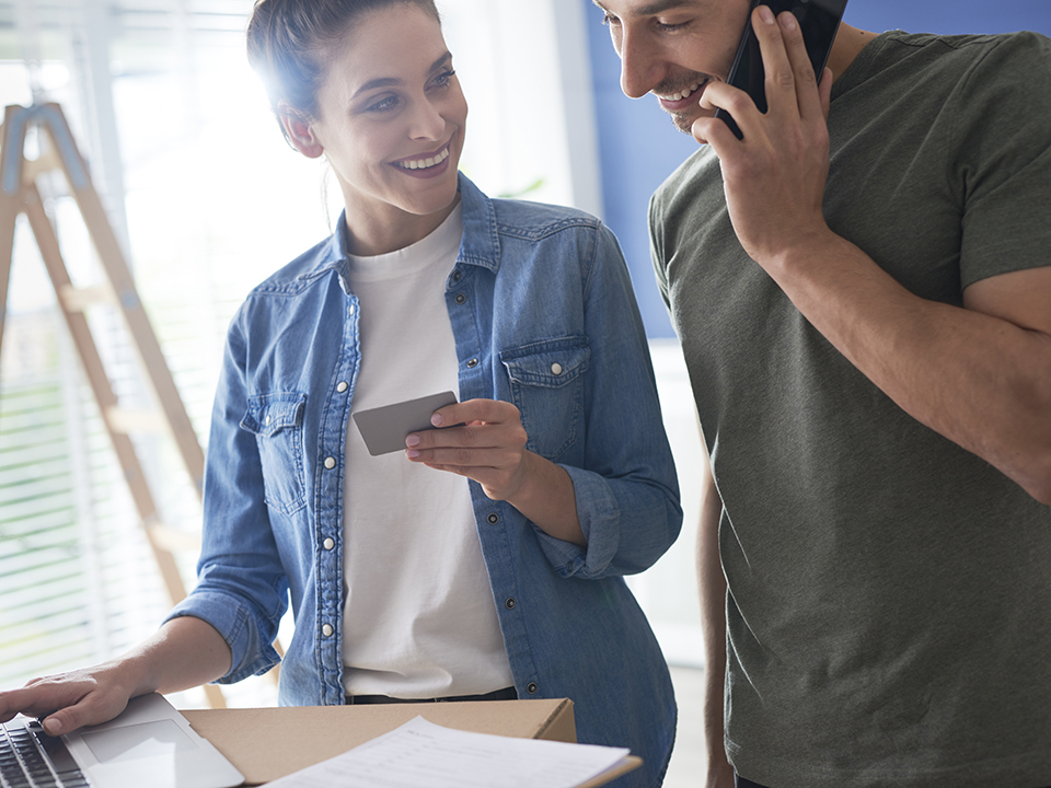 A man and woman working on home improvements. The man makes a call to the bank on his cell phone while the woman holds a credit card.