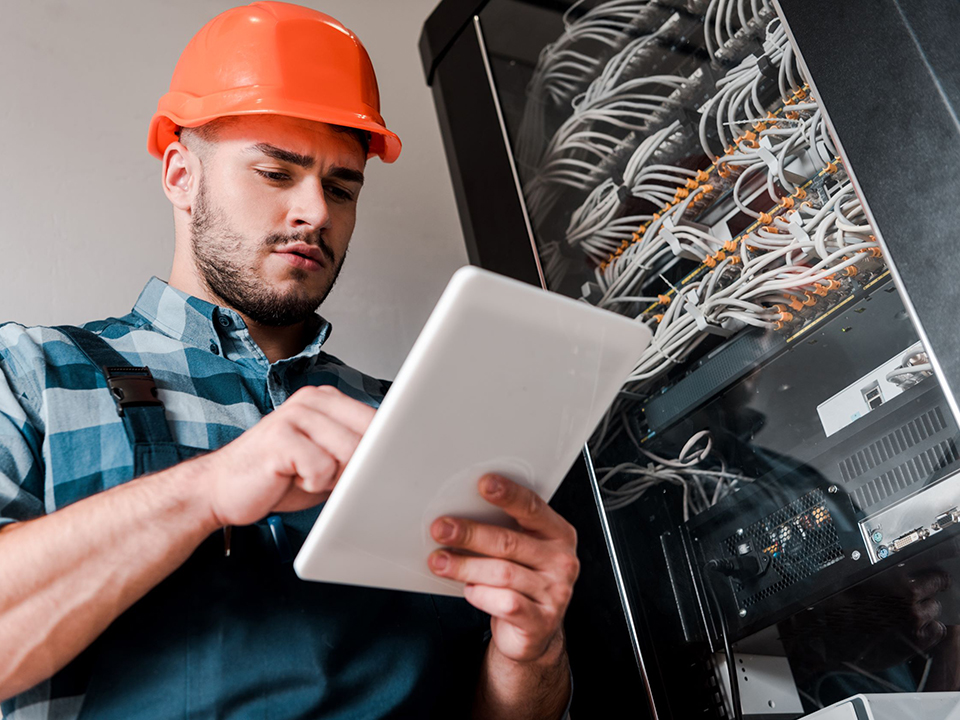 A low-angle view of a bearded technician using a tablet to examine cables.