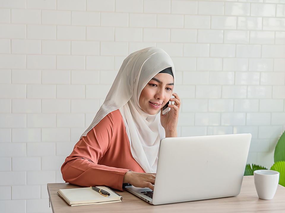 Woman using phone while sitting at her desk on her laptop