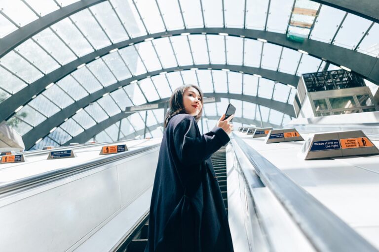 Young woman riding escalator with mobile device