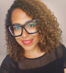 Headshot of a woman with curly hair wearing glasses and a black top, with a friendly smile.