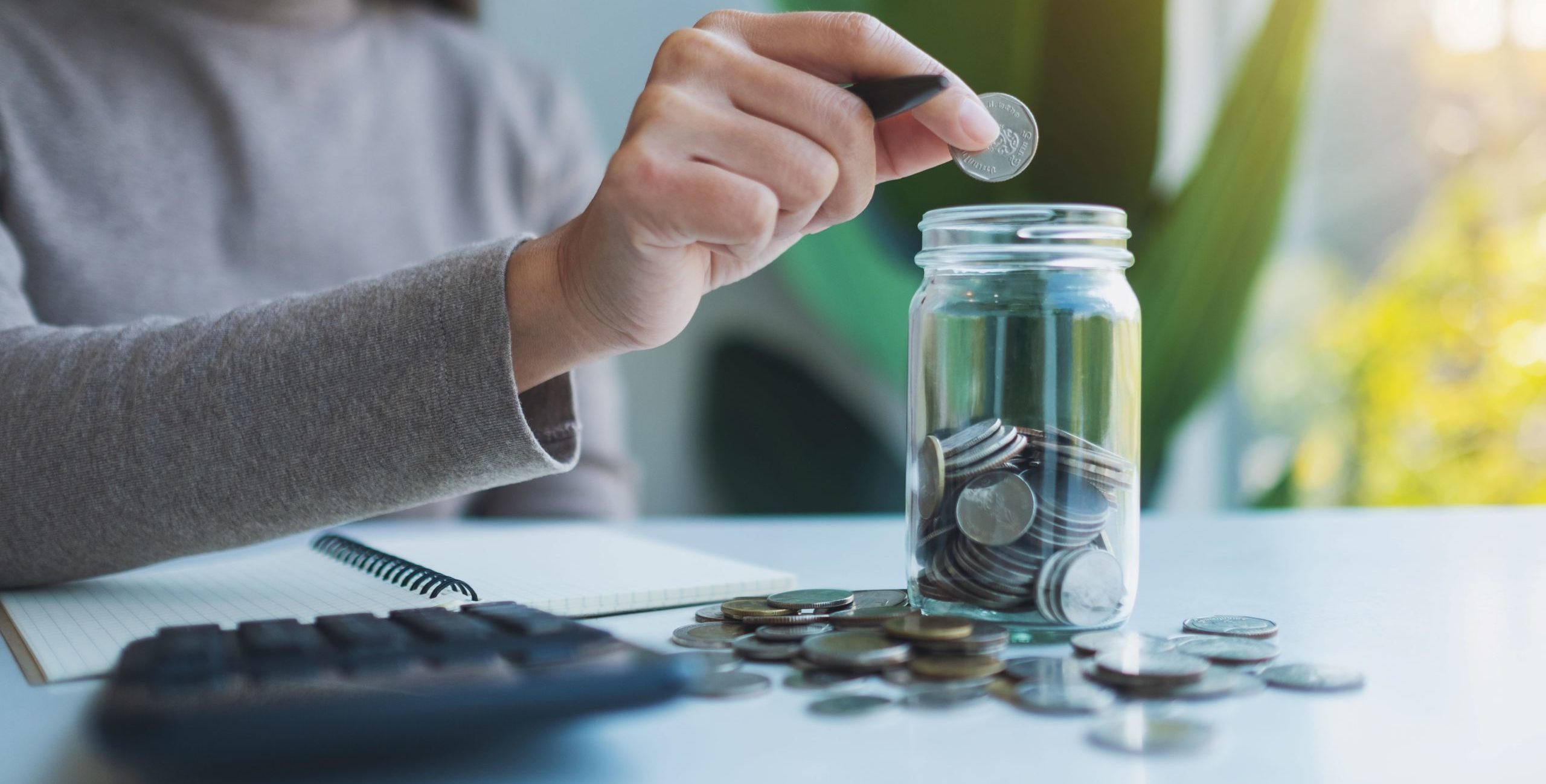 Hand putting a coin into a savings jar.