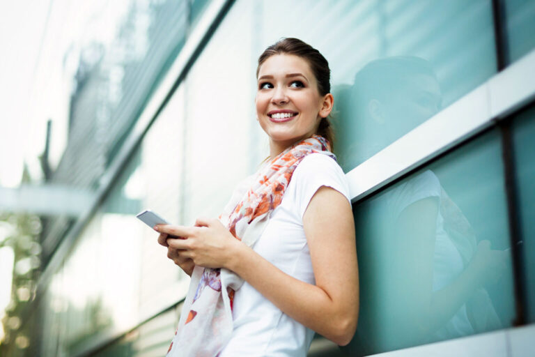 Young woman using smartphone outside next to building