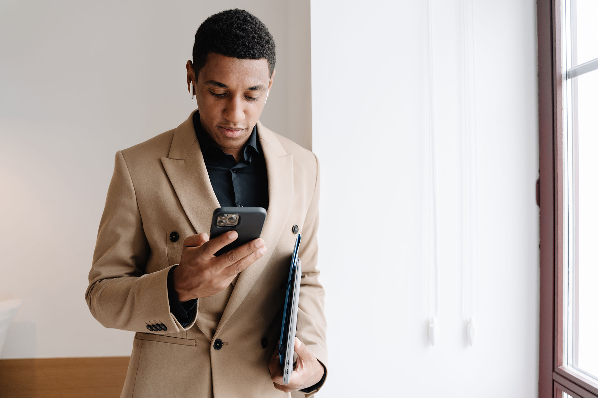 Black man wearing suit using cellphone and wireless earphones