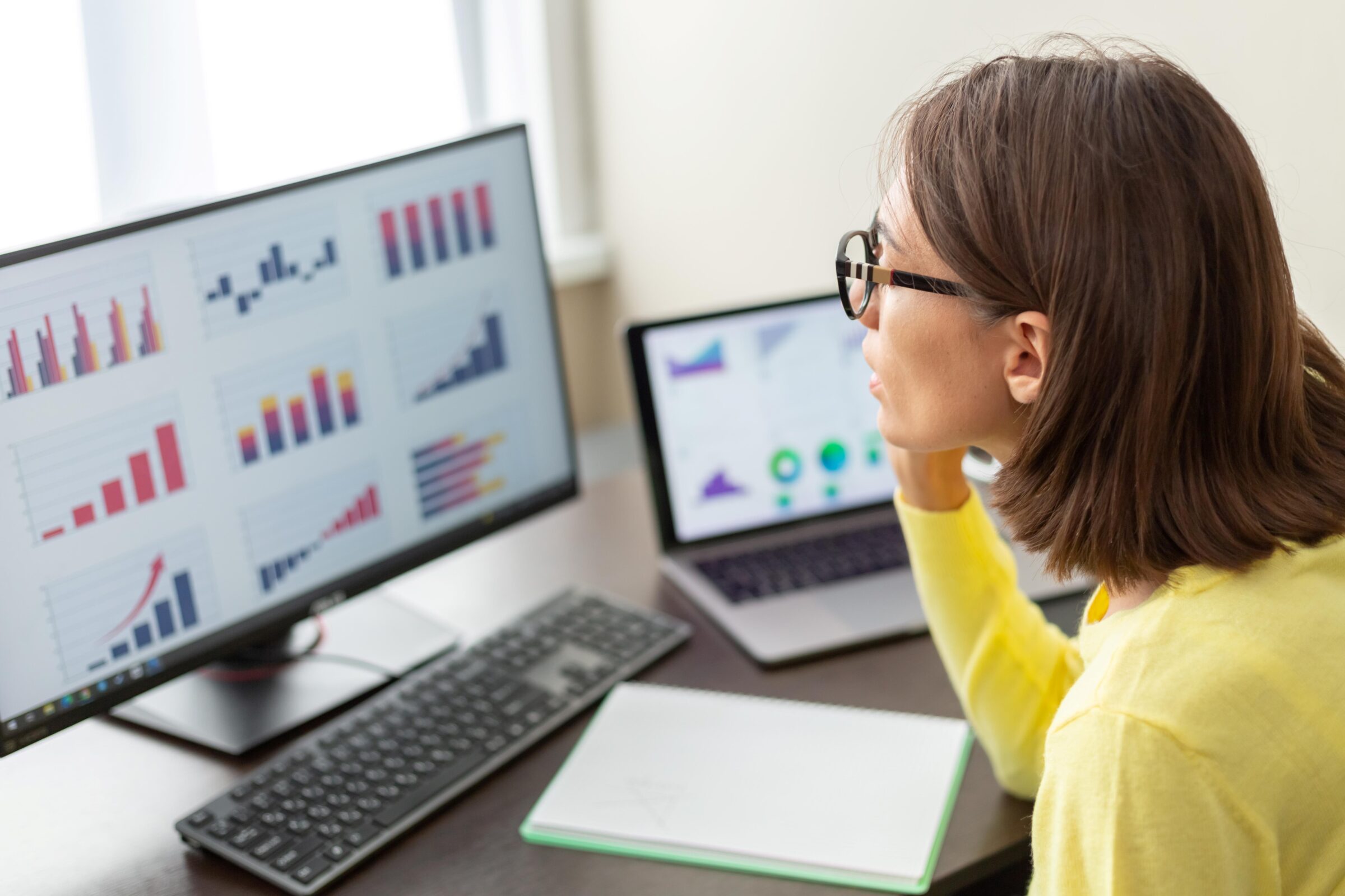 A young woman analyzes a series of charts on her desktop computer.