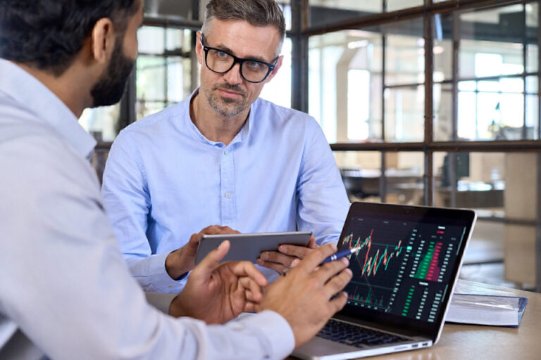 Diverse businessmen traders discussing cryptocurrency at desk using devices.