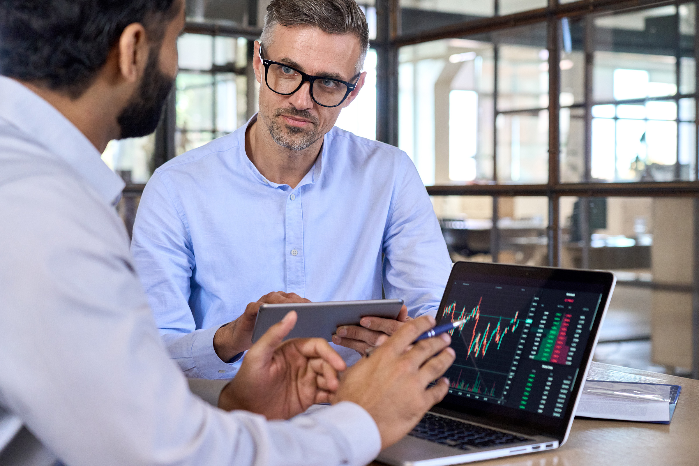 Diverse businessmen traders discussing cryptocurrency at desk using devices.