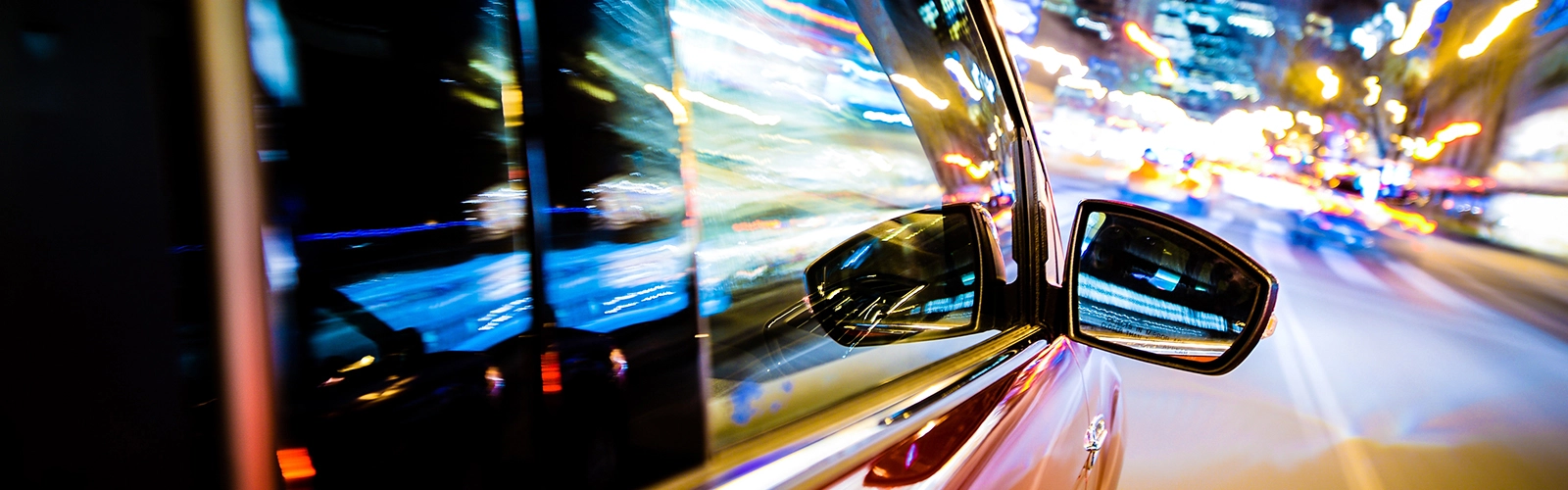 A car is driving through the city and lights are reflecting off of it.