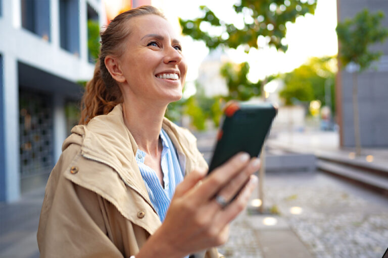 Handsome young smiling woman with mobile phone walking on the street