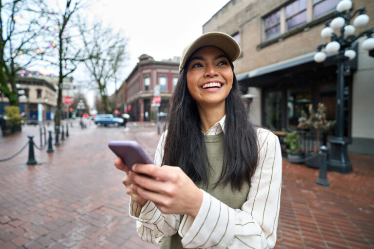 Happy Asian teen girl using smartphone standing on city street with smartphone.