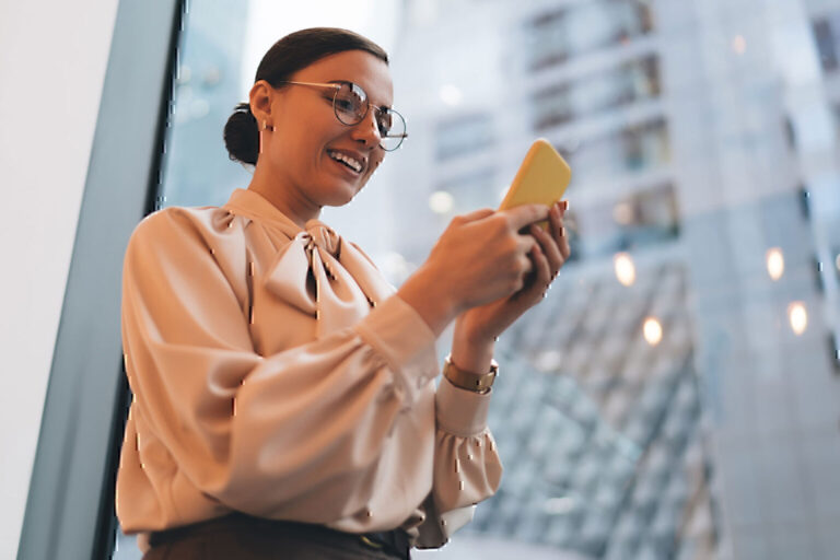 Happy female browsing cellphone standing near window