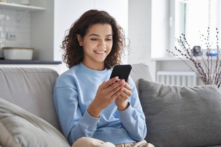 Happy hispanic teen girl holding cell phone using smartphone at home
