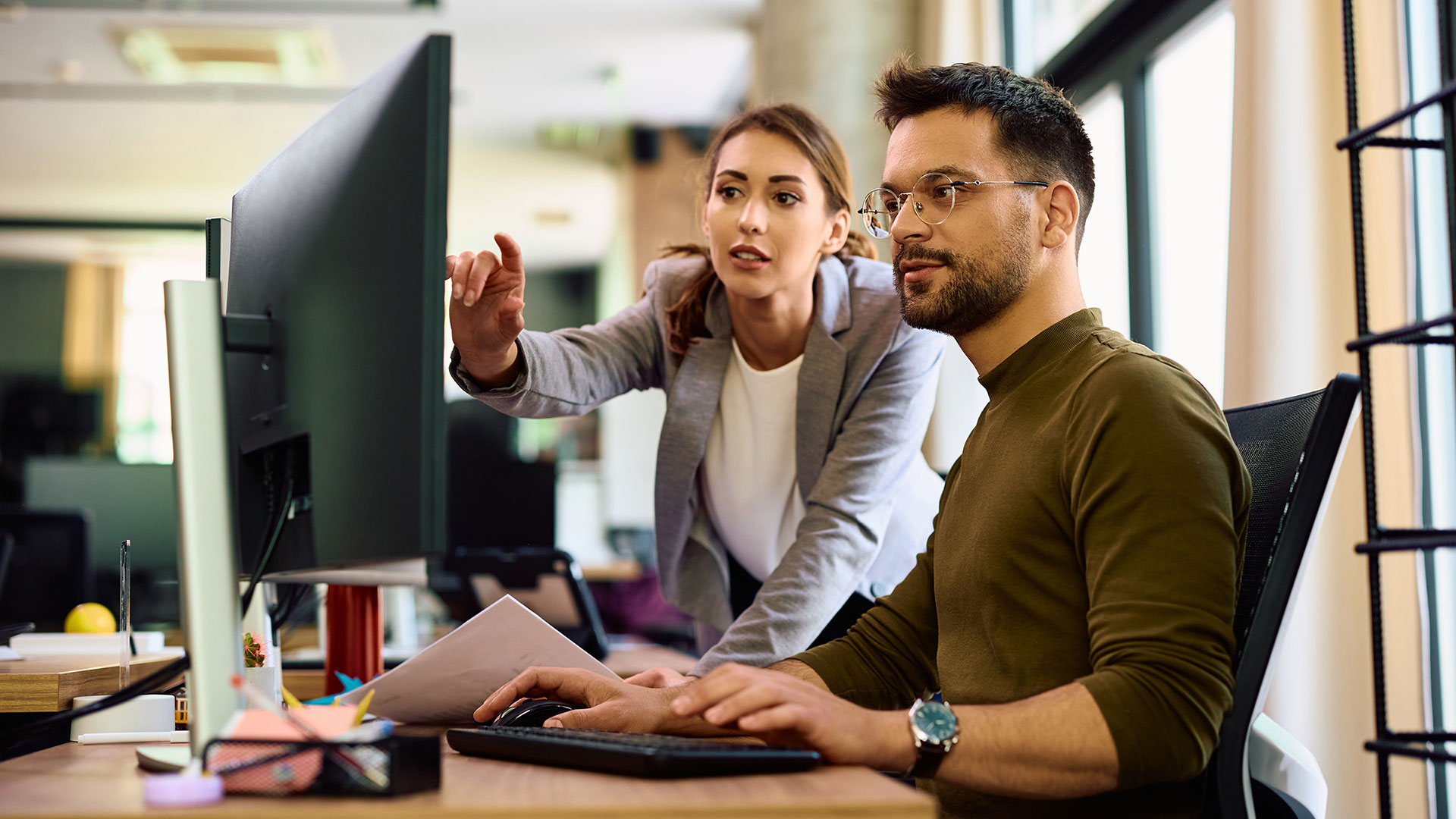 Young business colleagues collaborate around desktop PC while working in the office.