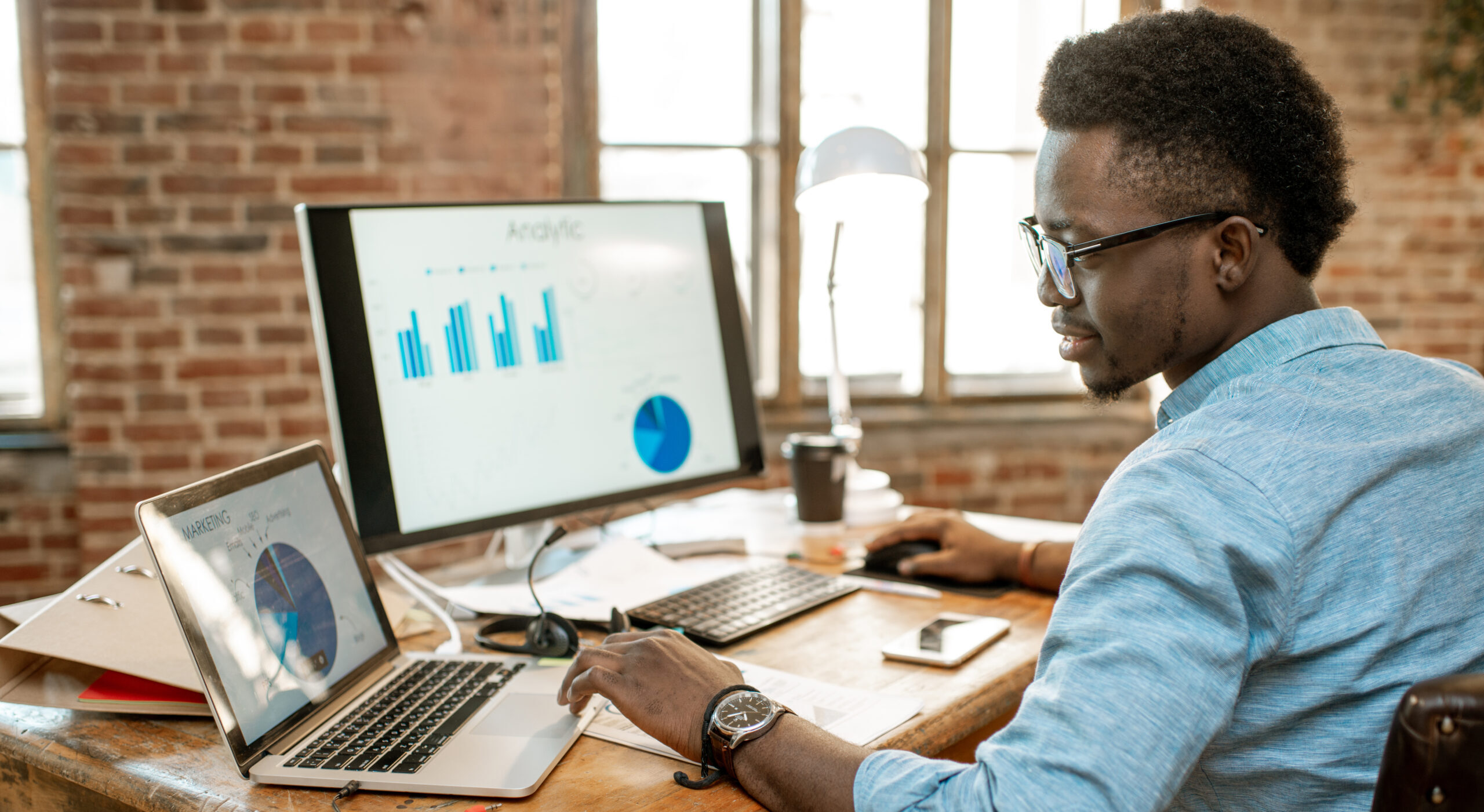 Man analyzing data on computer screens in a bright office.