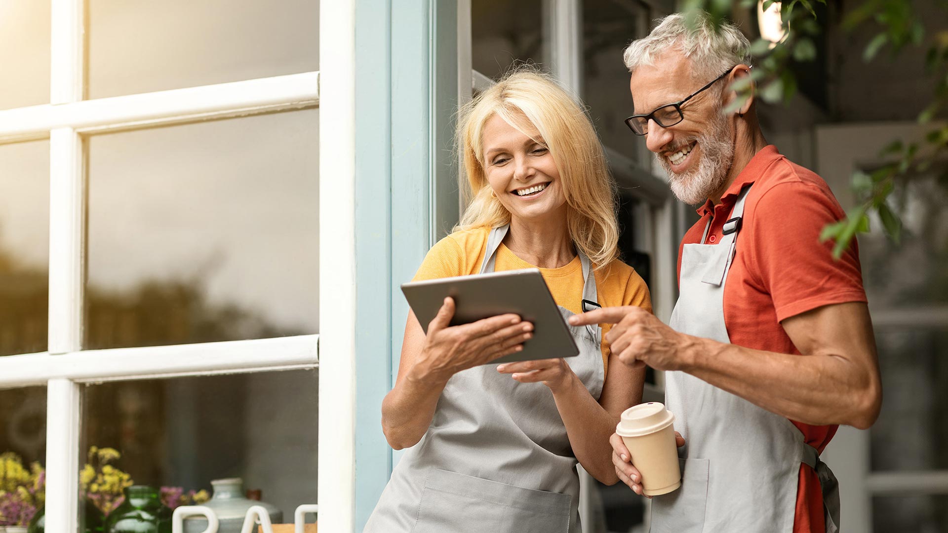 Smiling couple reviewing orders on tablet outside small business