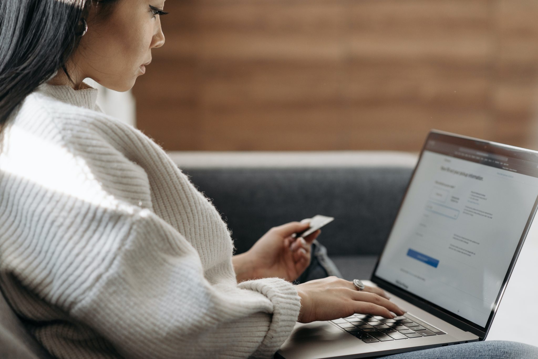 A young woman holding a credit card enters payment details on her laptop.
