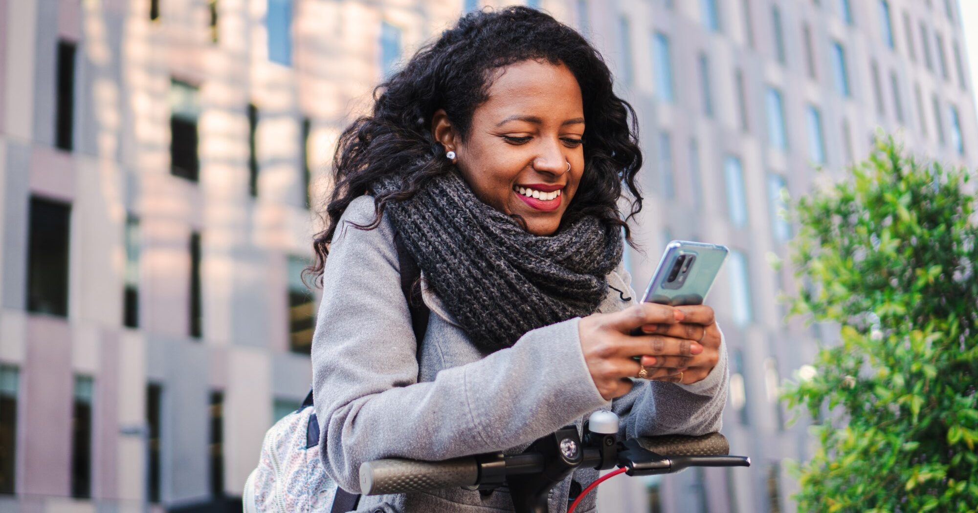 Woman smiling and using smartphone while on a scooter.